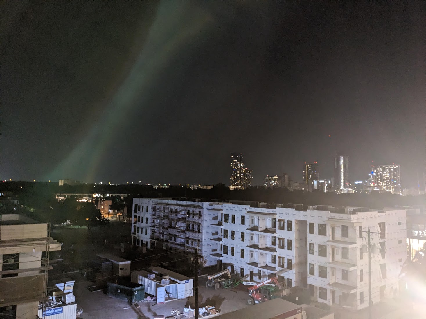 a blurry, distorted picture of a city. in the foreground is an apartment building. in the background is a set of sky scrapers. the sky above is dark, but no stars are visible.